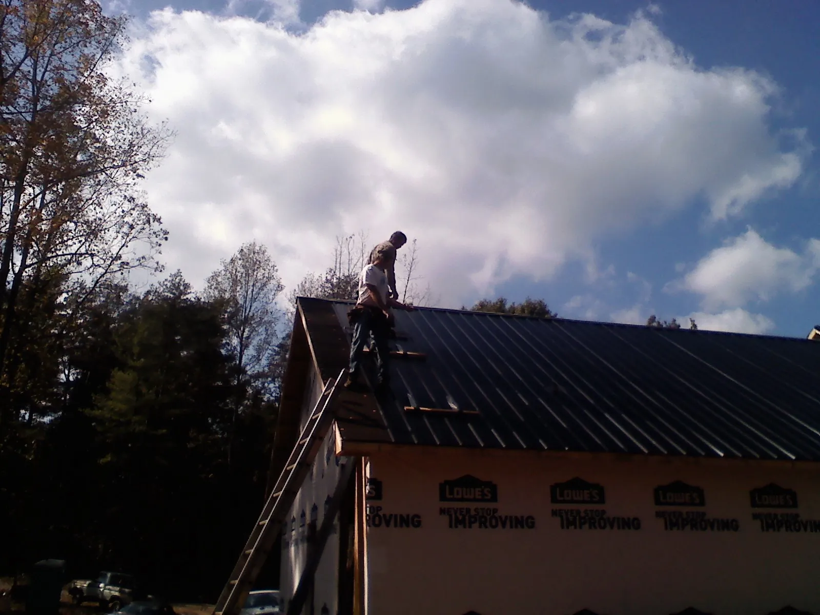 Roofer fastening dark metal panels high against a cloudy sky, from a Roof Inspection job in Clifton
